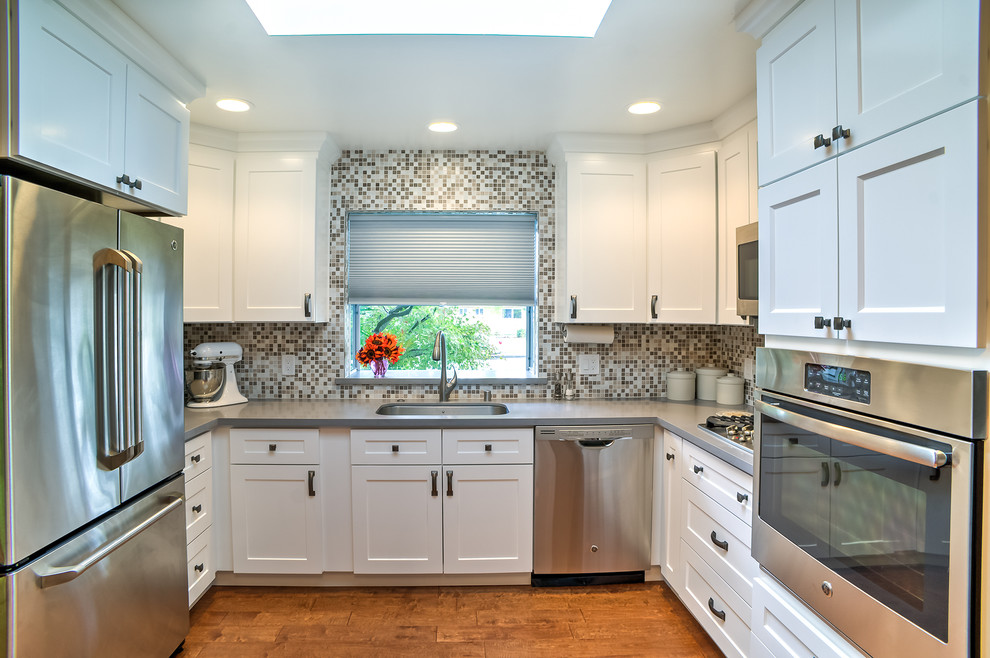 Inspiration for a small transitional u-shaped medium tone wood floor enclosed kitchen remodel in San Francisco with a single-bowl sink, shaker cabinets, white cabinets, quartz countertops, multicolored backsplash, stone tile backsplash, stainless steel appliances and no island