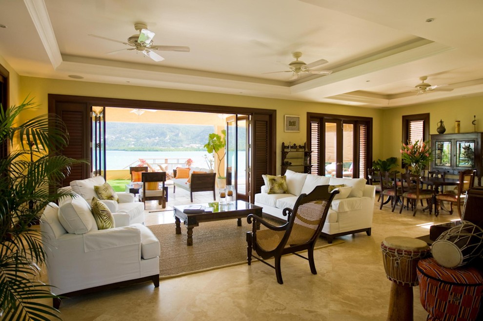 This is an example of a large tropical open concept living room in Other with beige walls and travertine floors.