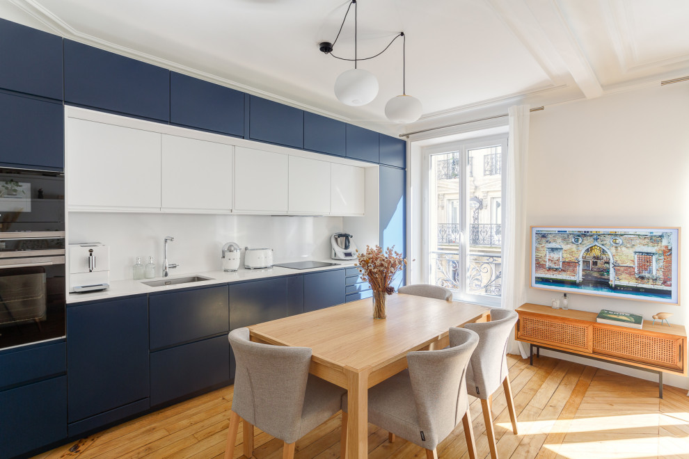 This is an example of a large contemporary galley open plan kitchen in Paris with a submerged sink, flat-panel cabinets, quartz worktops, integrated appliances, dark hardwood flooring, no island, white worktops, a vaulted ceiling and brown floors.