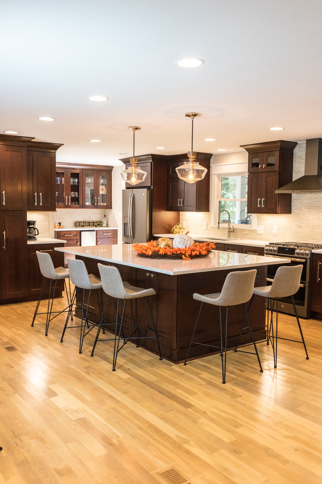 This is an example of a large transitional l-shaped kitchen in Atlanta with an undermount sink, shaker cabinets, dark wood cabinets, grey splashback, cement tile splashback, stainless steel appliances, light hardwood floors, with island, brown floor and white benchtop.