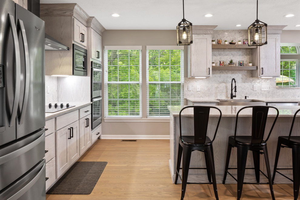 This is an example of a large country u-shaped eat-in kitchen in Cincinnati with a farmhouse sink, shaker cabinets, white cabinets, granite benchtops, white splashback, marble splashback, stainless steel appliances, light hardwood floors, multiple islands and white benchtop.