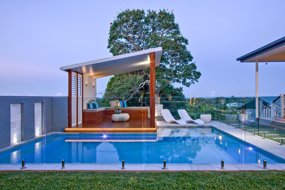 Photo of a mid-sized modern backyard custom-shaped aboveground pool in Brisbane with a pool house and natural stone pavers.