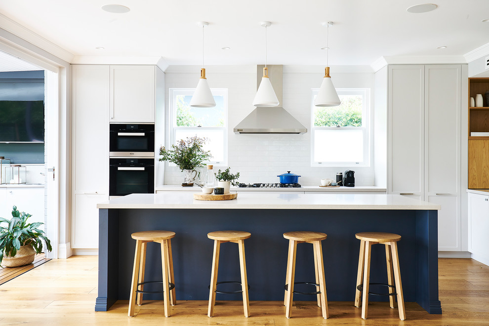 Design ideas for a large transitional l-shaped open plan kitchen in Sydney with an undermount sink, shaker cabinets, white cabinets, quartz benchtops, white splashback, subway tile splashback, stainless steel appliances, medium hardwood floors, with island and brown floor.