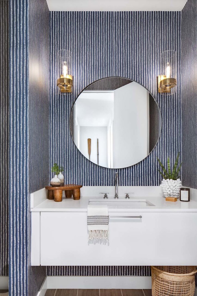 Inspiration for a beach style powder room in Orange County with flat-panel cabinets, white cabinets, blue walls, an undermount sink, brown floor, white benchtops and solid surface benchtops.
