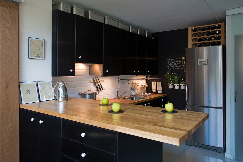 Photo of a mid-sized transitional u-shaped separate kitchen in Madrid with a drop-in sink, flat-panel cabinets, black cabinets, wood benchtops, white splashback, subway tile splashback, stainless steel appliances and a peninsula.