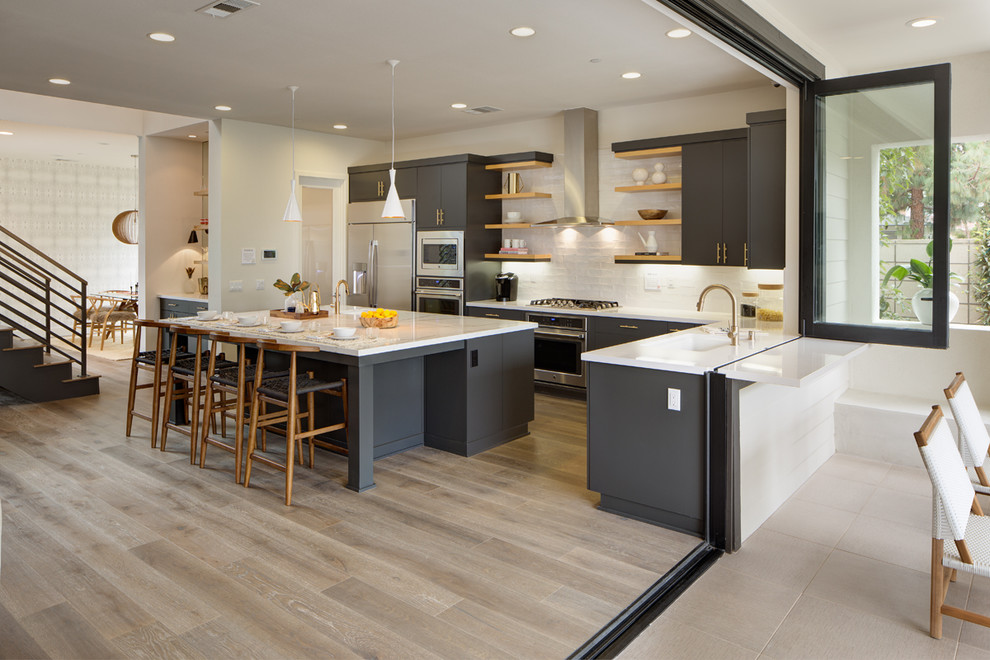 Design ideas for a contemporary l-shaped open plan kitchen in Los Angeles with an undermount sink, flat-panel cabinets, grey cabinets, white splashback, subway tile splashback, light hardwood floors and with island.