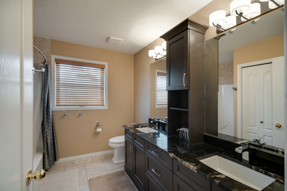 Mid-sized modern master bathroom in Edmonton with shaker cabinets, dark wood cabinets, a shower/bathtub combo, a one-piece toilet, beige walls, an undermount sink, granite benchtops and a shower curtain.