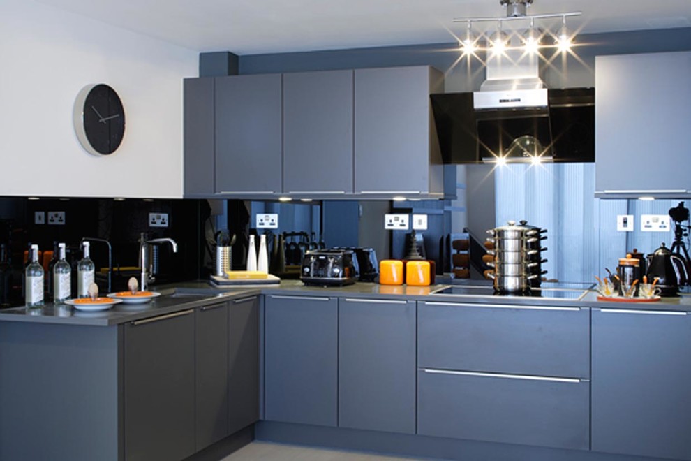 Mid-sized industrial l-shaped open plan kitchen in Surrey with a single-bowl sink, shaker cabinets, grey cabinets, glass benchtops, black splashback and no island.