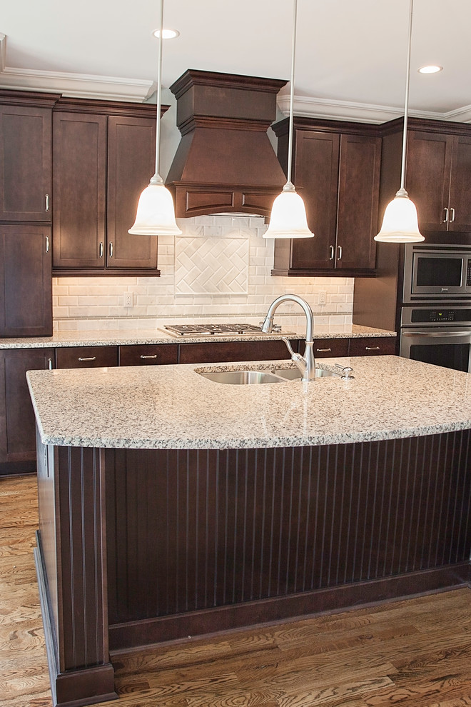 This is an example of a traditional l-shaped eat-in kitchen in Other with an undermount sink, brown cabinets, granite benchtops, white splashback, stainless steel appliances and with island.