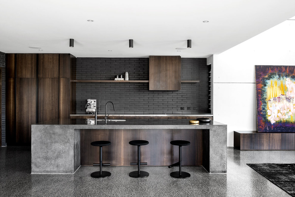 Expansive industrial galley open plan kitchen in Brisbane with an undermount sink, flat-panel cabinets, dark wood cabinets, concrete benchtops, black splashback, brick splashback, concrete floors, with island and grey floor.