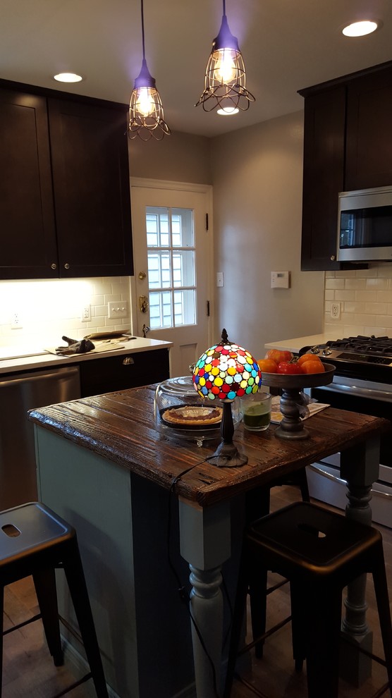 Inspiration for a mid-sized rustic u-shaped porcelain tile eat-in kitchen remodel in Indianapolis with a farmhouse sink, shaker cabinets, dark wood cabinets, wood countertops, white backsplash, ceramic backsplash, stainless steel appliances and an island