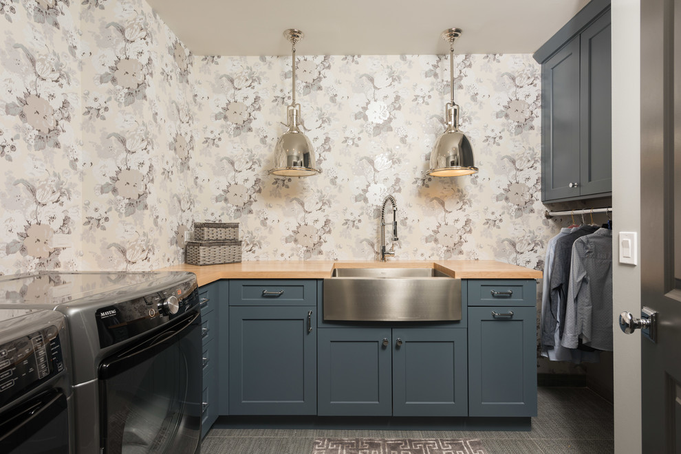 Design ideas for a large transitional u-shaped dedicated laundry room in Chicago with a farmhouse sink, blue cabinets, wood benchtops, porcelain floors, a side-by-side washer and dryer, grey floor, shaker cabinets, multi-coloured walls and beige benchtop.