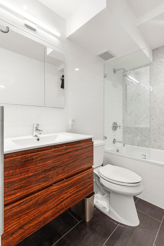 Small transitional master bathroom in New York with flat-panel cabinets, medium wood cabinets, a drop-in tub, a shower/bathtub combo, a two-piece toilet, white tile, ceramic tile, white walls, porcelain floors, an integrated sink, solid surface benchtops, grey floor, an open shower and white benchtops.