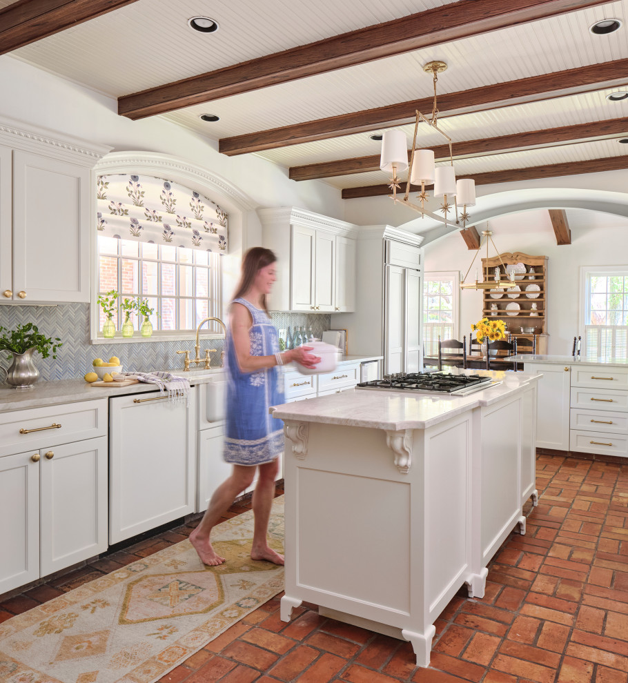 This is an example of a traditional l-shaped eat-in kitchen in Austin with a farmhouse sink, recessed-panel cabinets, white cabinets, marble benchtops, blue splashback, glass tile splashback, panelled appliances, terra-cotta floors, with island, white benchtop and exposed beam.
