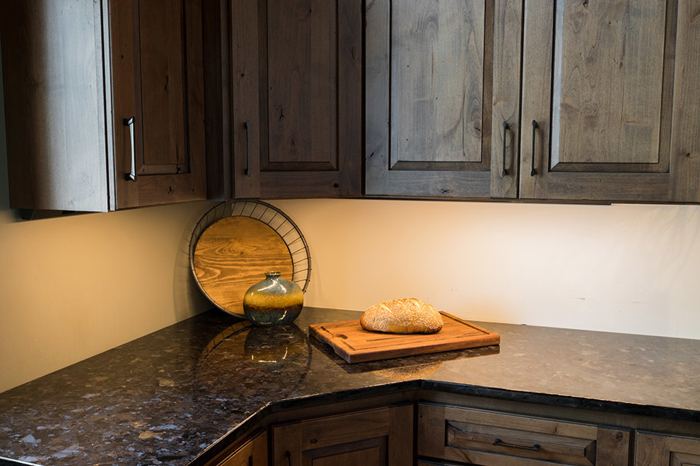 Example of a mountain style kitchen design with raised-panel cabinets, distressed cabinets, granite countertops and black countertops
