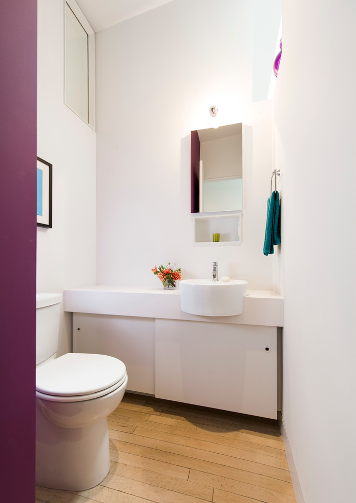 Photo of a scandinavian powder room in DC Metro with flat-panel cabinets, white cabinets, a two-piece toilet, white walls, medium hardwood floors and white benchtops.