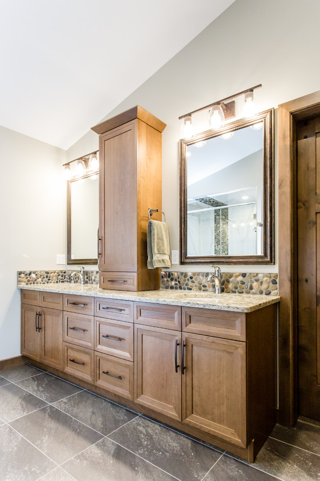 Inspiration for a mid-sized country master bathroom in Calgary with recessed-panel cabinets, light wood cabinets, a corner shower, a one-piece toilet, brown tile, pebble tile, grey walls, ceramic floors, an undermount sink, engineered quartz benchtops, brown floor, a hinged shower door and beige benchtops.