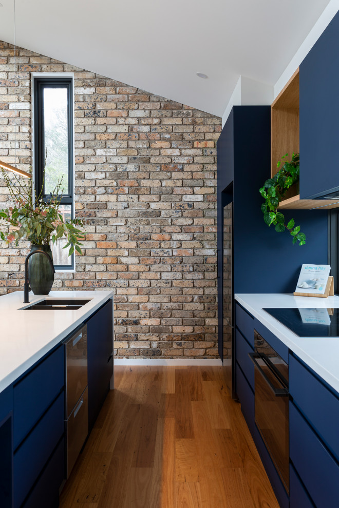 Immagine di una cucina contemporanea di medie dimensioni con lavello sottopiano, ante blu, top in quarzo composito, paraspruzzi a finestra, elettrodomestici neri, pavimento in legno massello medio e top bianco