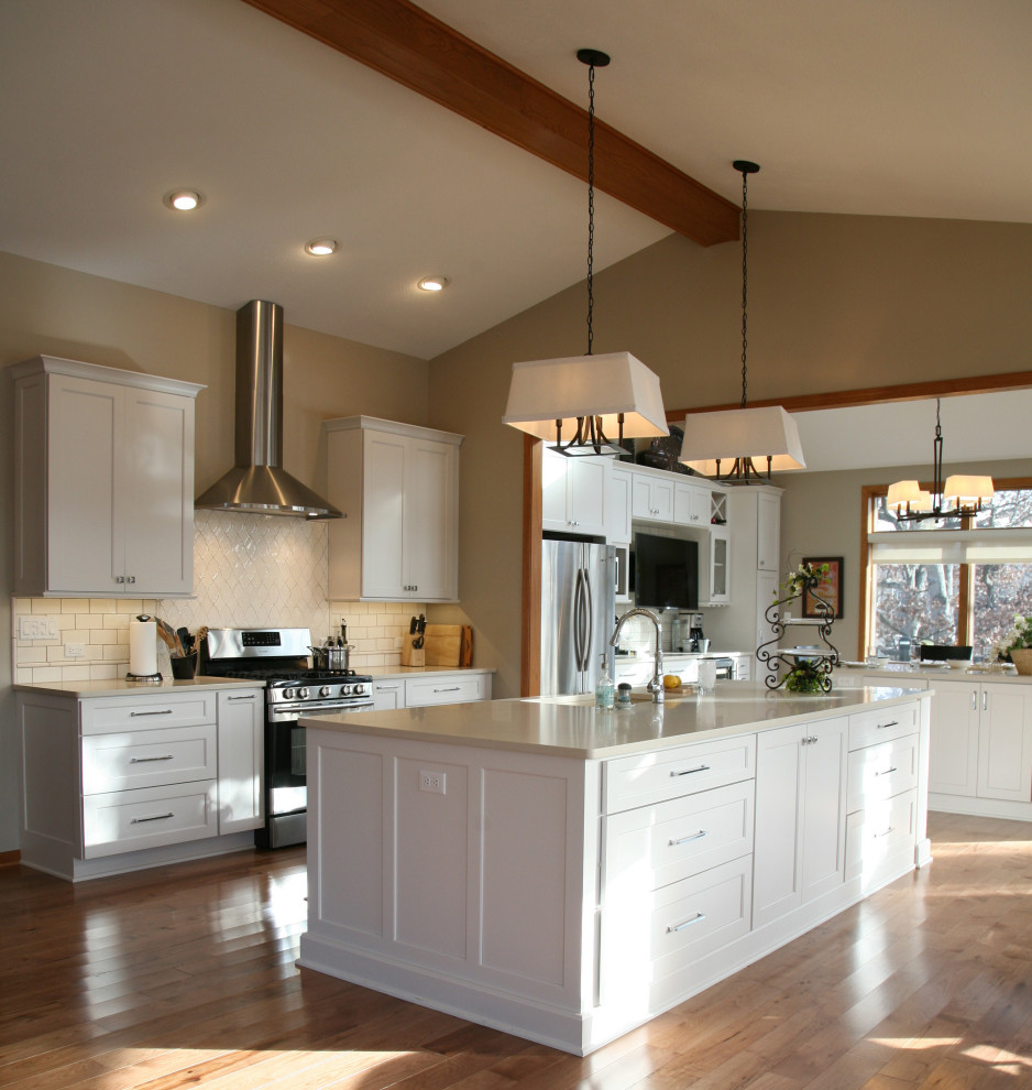Photo of a large nautical kitchen/diner in Milwaukee with a submerged sink, shaker cabinets, white cabinets, engineered stone countertops, white splashback, porcelain splashback, stainless steel appliances, light hardwood flooring, multiple islands, brown floors, white worktops and a vaulted ceiling.