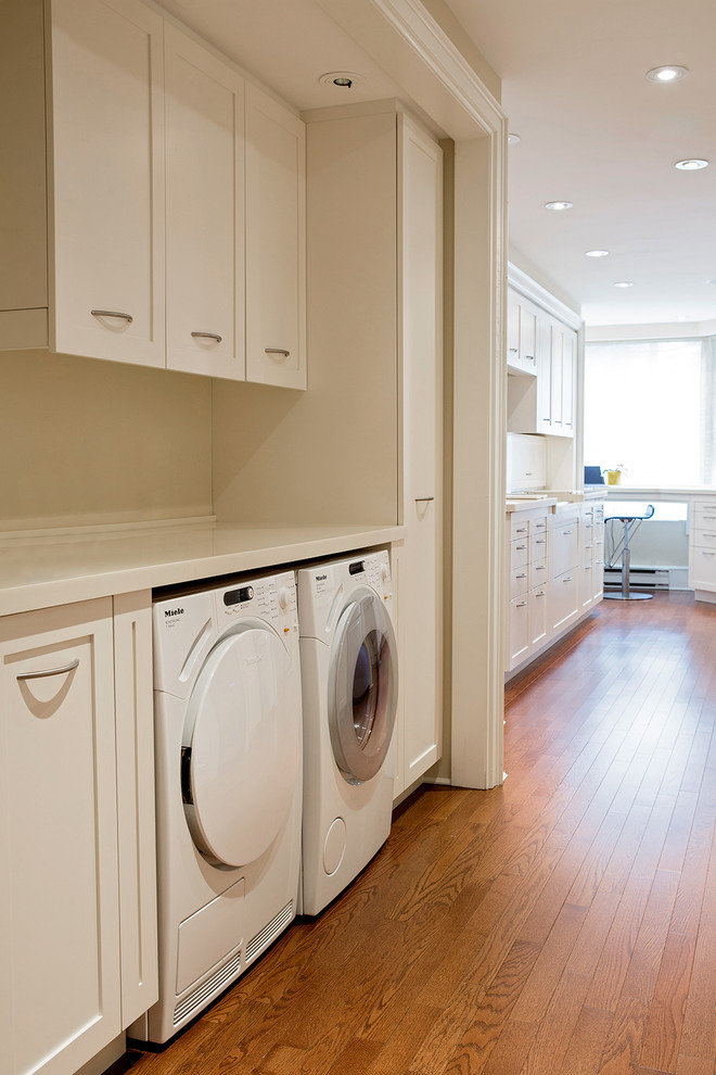 This is an example of a small transitional galley dedicated laundry room in Toronto with an undermount sink, shaker cabinets, white cabinets, solid surface benchtops, yellow walls, light hardwood floors and a side-by-side washer and dryer.