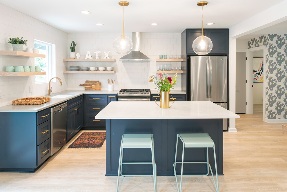 Photo of a mid-sized midcentury l-shaped eat-in kitchen in Austin with an undermount sink, shaker cabinets, blue cabinets, white splashback, subway tile splashback, stainless steel appliances, light hardwood floors, with island, beige floor, white benchtop and solid surface benchtops.
