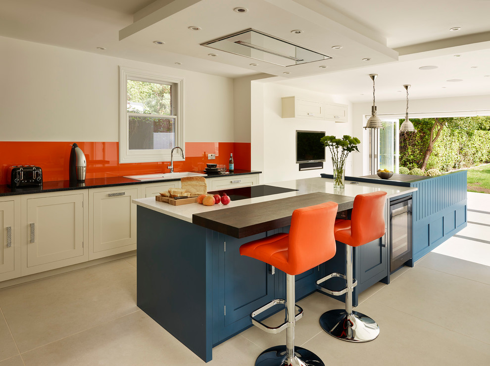 Inspiration for a transitional kitchen in London with a drop-in sink, shaker cabinets, orange splashback, glass sheet splashback and with island.