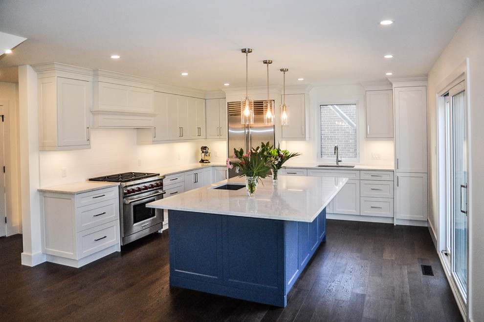 Example of a large transitional l-shaped dark wood floor and brown floor open concept kitchen design with an undermount sink, shaker cabinets, white cabinets, quartzite countertops, white backsplash, ceramic backsplash, stainless steel appliances and an island