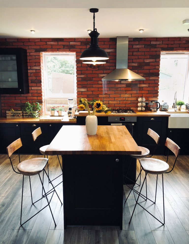 Large industrial l-shaped open plan kitchen in Other with a farmhouse sink, raised-panel cabinets, black cabinets, wood benchtops, black appliances, dark hardwood floors, with island, multi-coloured floor, brown benchtop and recessed.