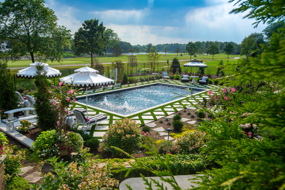 Modelo de piscina alargada clásica de tamaño medio rectangular en patio trasero con paisajismo de piscina y adoquines de piedra natural