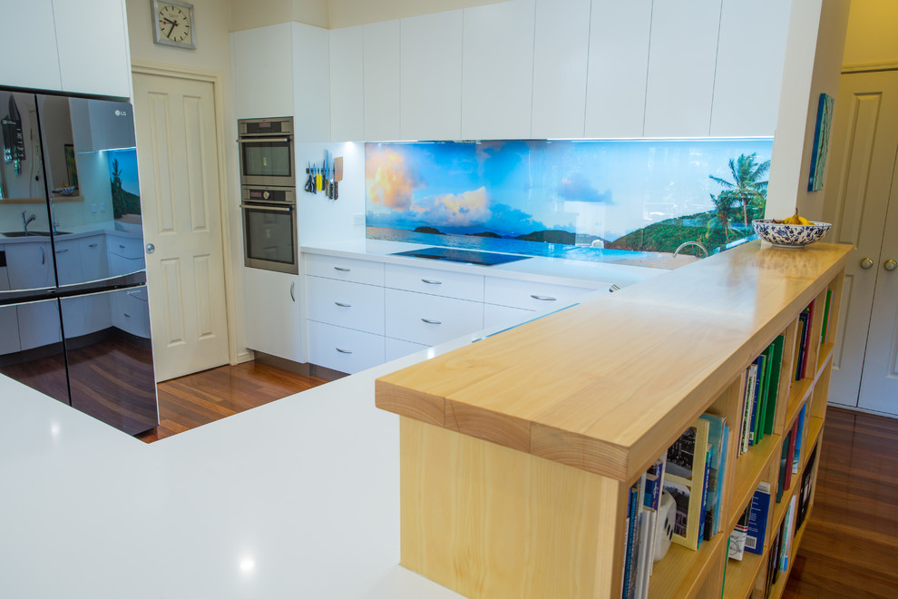 This is an example of a mid-sized beach style u-shaped kitchen pantry in Brisbane with a double-bowl sink, flat-panel cabinets, blue cabinets, quartz benchtops, blue splashback, glass sheet splashback, stainless steel appliances, dark hardwood floors, with island, brown floor and white benchtop.