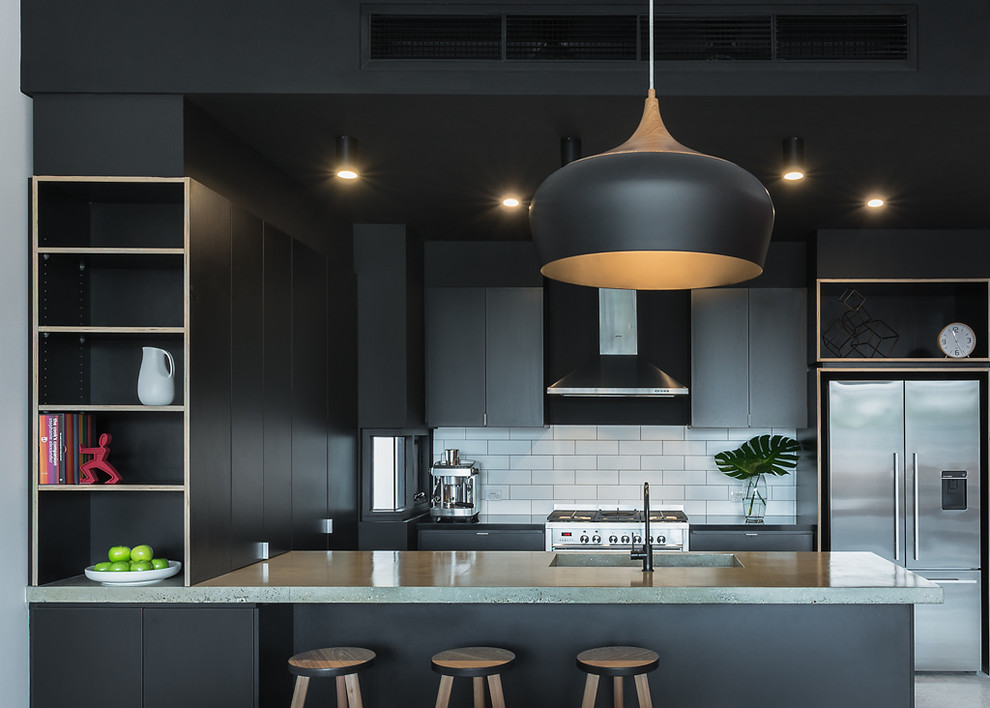 Small industrial u-shaped open plan kitchen in Melbourne with an integrated sink, black cabinets, concrete benchtops, white splashback, subway tile splashback, stainless steel appliances, concrete floors and a peninsula.