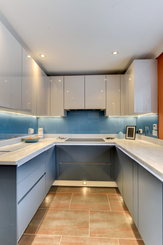 This is an example of a large modern u-shaped eat-in kitchen in Sussex with a drop-in sink, flat-panel cabinets, blue cabinets, solid surface benchtops, blue splashback, glass sheet splashback, panelled appliances, vinyl floors, no island, brown floor and white benchtop.