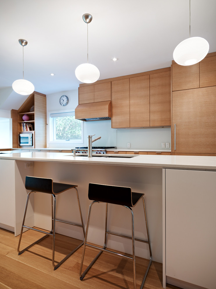 Photo of a modern galley eat-in kitchen in Toronto with an undermount sink, flat-panel cabinets, light wood cabinets, white splashback, glass sheet splashback, stainless steel appliances, light hardwood floors and with island.