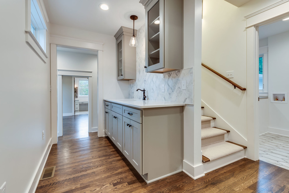 This is an example of a small country single-wall wet bar in Nashville with a drop-in sink, shaker cabinets, grey cabinets, quartz benchtops, white splashback, marble splashback, medium hardwood floors, brown floor and white benchtop.