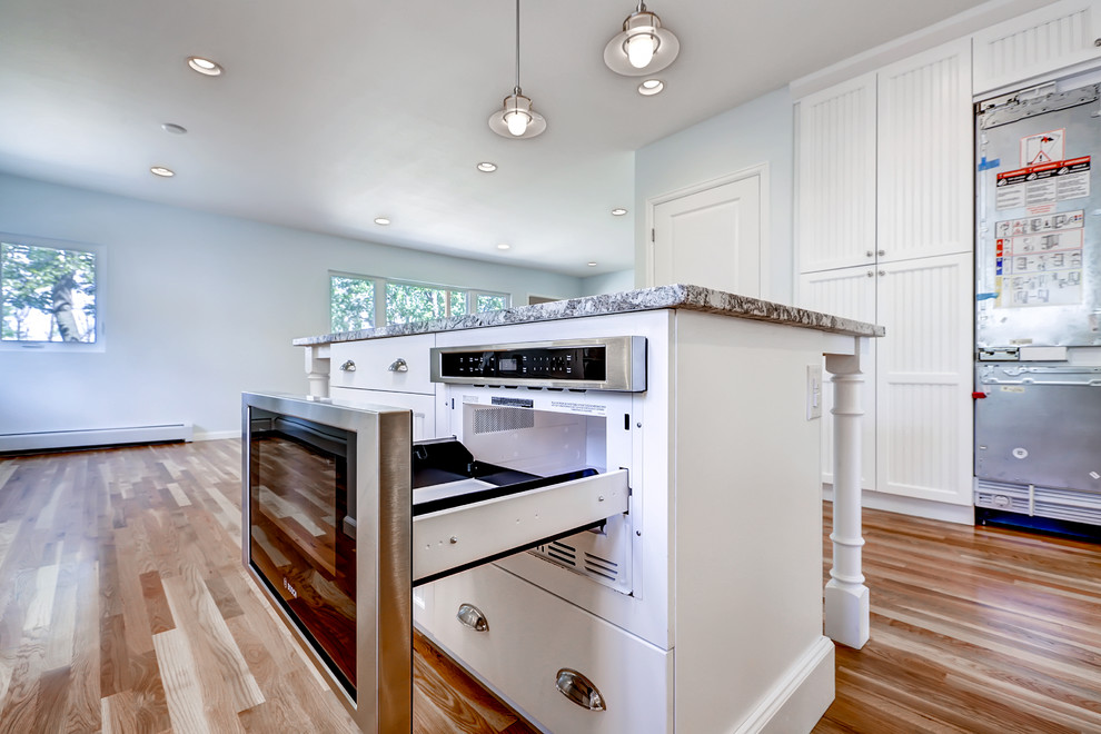 This is an example of a large country galley open plan kitchen in Denver with white cabinets, with island, a drop-in sink, white splashback, metal splashback, stainless steel appliances and medium hardwood floors.