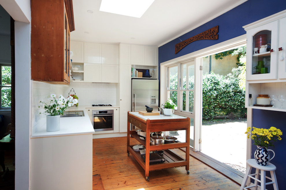 This is an example of a mid-sized country l-shaped eat-in kitchen in Sydney with shaker cabinets, white splashback, ceramic splashback, stainless steel appliances, medium hardwood floors and with island.