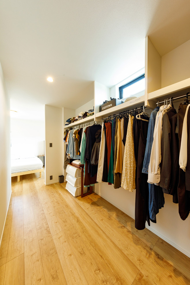 Ejemplo de armario vestidor unisex industrial de tamaño medio con armarios abiertos, puertas de armario blancas, suelo de madera en tonos medios, suelo marrón y papel pintado