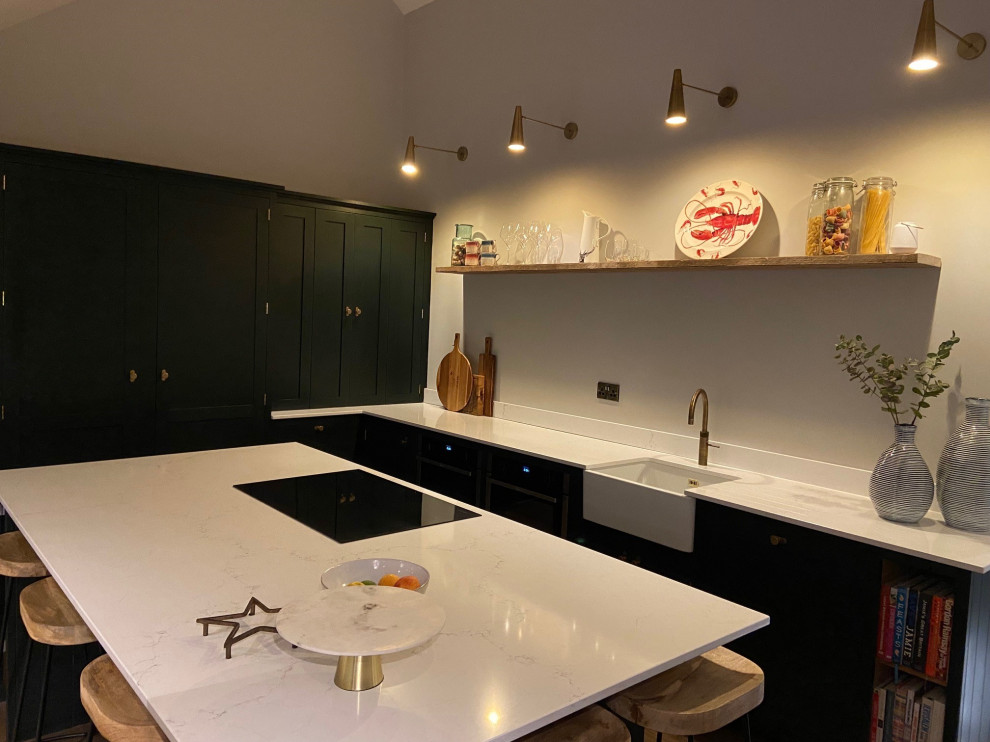 Große Moderne Wohnküche mit Landhausspüle, Kassettenfronten, Quarzwerkstein-Arbeitsplatte, schwarzen Elektrogeräten, Kücheninsel, braunem Boden und weißer Arbeitsplatte in Surrey