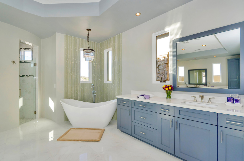 Photo of a large contemporary master bathroom in Phoenix with shaker cabinets, blue cabinets, a freestanding tub, an alcove shower, green tile, matchstick tile, grey walls, marble floors, an undermount sink and white floor.