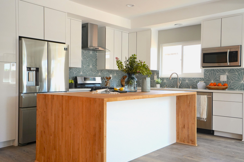 Bild på ett funkis vit vitt u-kök, med en undermonterad diskho, släta luckor, vita skåp, bänkskiva i kvarts, blått stänkskydd, rostfria vitvaror, mellanmörkt trägolv, en köksö och brunt golv