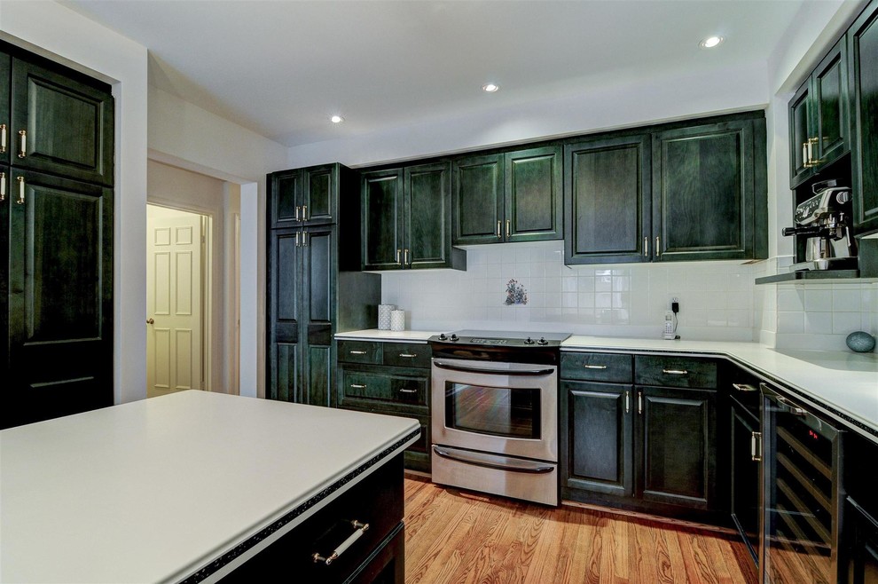 Inspiration for a large transitional l-shaped medium tone wood floor and brown floor enclosed kitchen remodel in Toronto with a double-bowl sink, recessed-panel cabinets, green cabinets, laminate countertops, white backsplash, ceramic backsplash, stainless steel appliances and an island