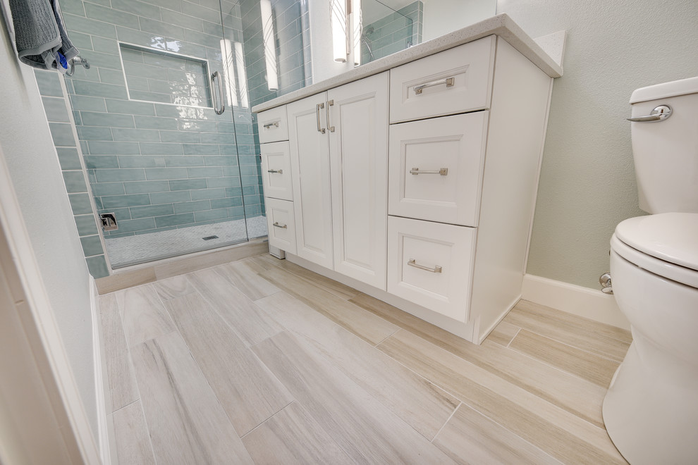 This is an example of a mid-sized transitional kids bathroom in Portland with raised-panel cabinets, white cabinets, an alcove shower, a two-piece toilet, blue tile, subway tile, blue walls, porcelain floors, an undermount sink, engineered quartz benchtops, brown floor, a hinged shower door and white benchtops.
