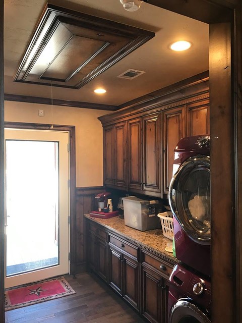 Example of a small transitional galley dark wood floor and brown floor dedicated laundry room design in Dallas with raised-panel cabinets, light wood cabinets, granite countertops, beige walls, a stacked washer/dryer and beige countertops
