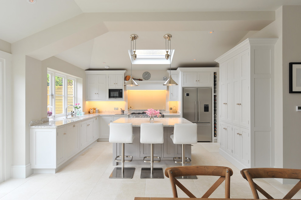 This is an example of a mid-sized transitional u-shaped eat-in kitchen in London with recessed-panel cabinets, granite benchtops, stainless steel appliances, limestone floors and with island.