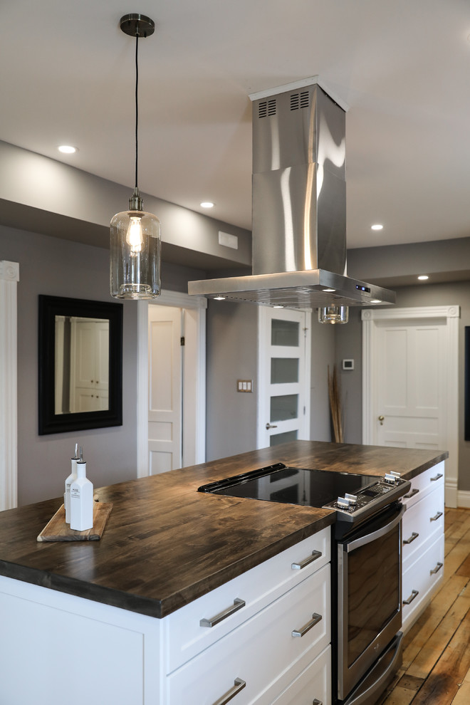 Mid-sized transitional single-wall medium tone wood floor and brown floor eat-in kitchen photo with a farmhouse sink, shaker cabinets, white cabinets, white backsplash, stainless steel appliances, an island and white countertops