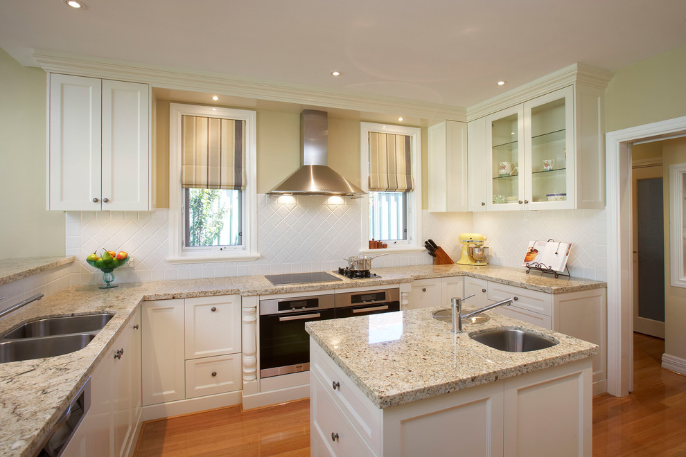 This is an example of a traditional u-shaped kitchen in Perth with an undermount sink, shaker cabinets, white cabinets, granite benchtops, white splashback, porcelain splashback, stainless steel appliances, with island, multi-coloured benchtop and medium hardwood floors.