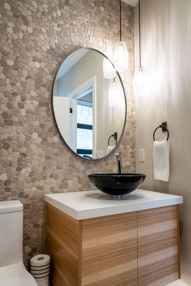 Small contemporary powder room in Other with flat-panel cabinets, light wood cabinets, a one-piece toilet, beige tile, pebble tile, beige walls, pebble tile floors, a vessel sink, engineered quartz benchtops, beige floor and white benchtops.