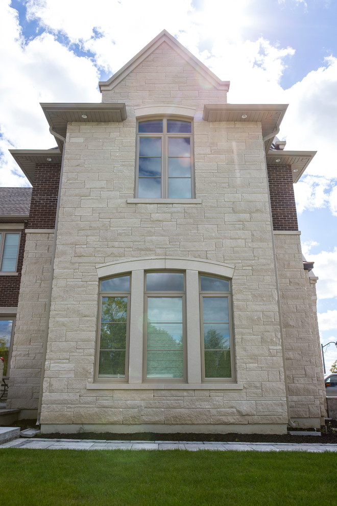 This is an example of a large transitional two-storey beige exterior in Toronto with stone veneer and a gable roof.