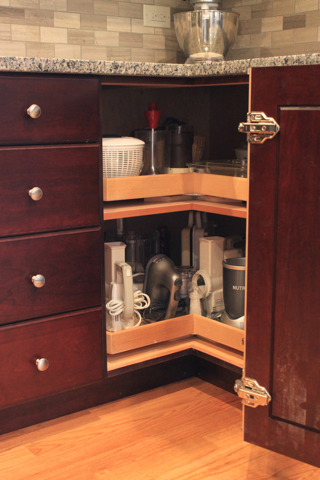 Example of a mid-sized transitional u-shaped laminate floor eat-in kitchen design with an undermount sink, raised-panel cabinets, dark wood cabinets, quartz countertops, gray backsplash, porcelain backsplash, stainless steel appliances and no island