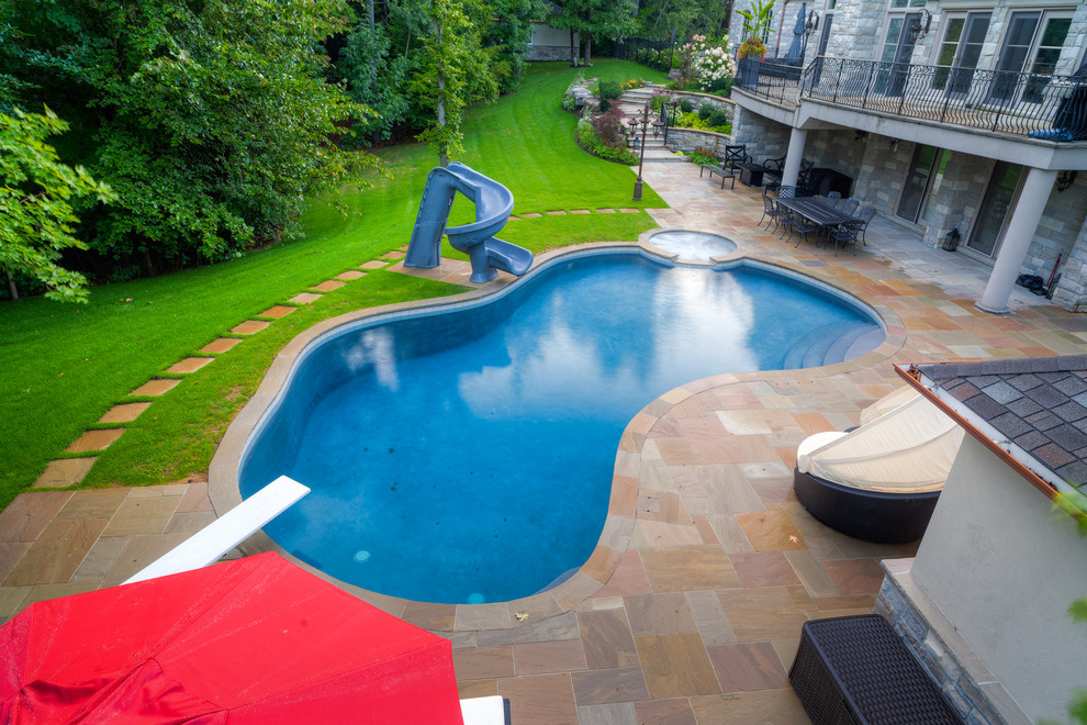 Design ideas for a large traditional backyard custom-shaped pool in Other with a water slide and natural stone pavers.